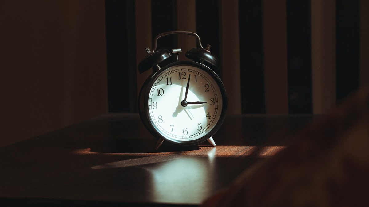 A classic alarm clock on a wooden nightstand in early morning light