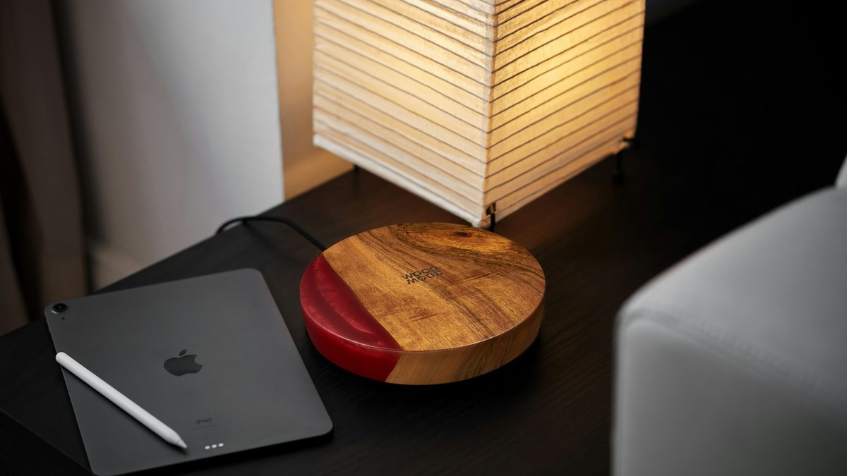 An iPad and a wooden charging dock on a bedside table under a paper lamp