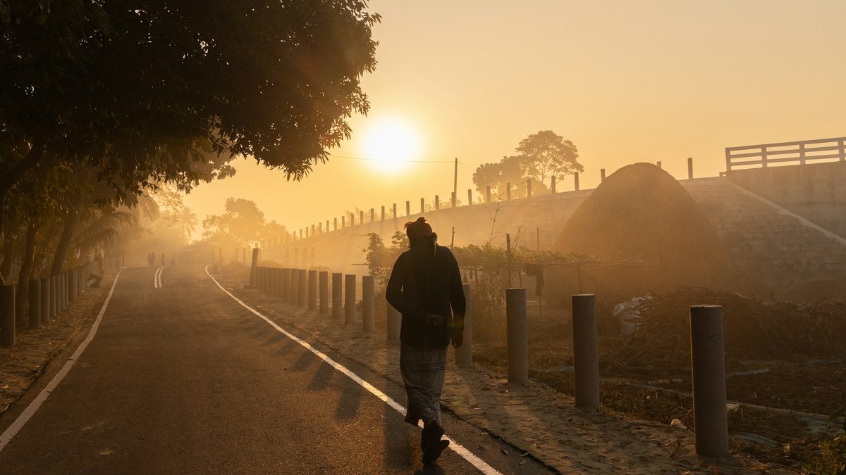 A person walking along a misty path at sunrise, the sun low and golden