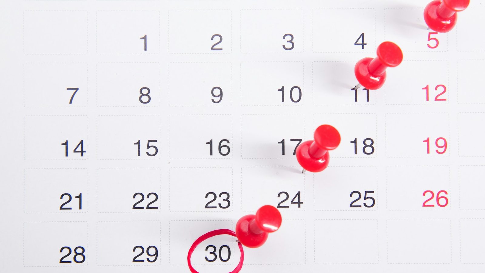 Un calendrier mural avec des punaises rouges et une date entourée de rouge