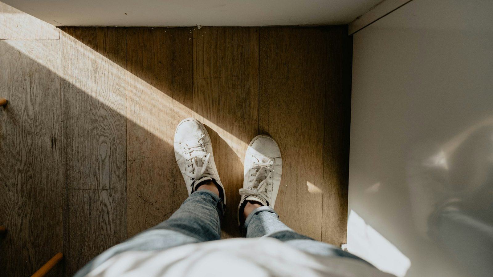 Feet in white sneakers standing on a wooden floor beside the bed