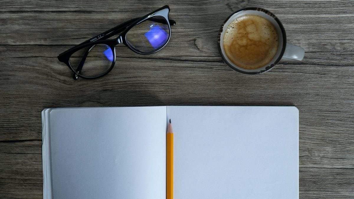 An open notebook with a pencil and a cup of coffee on a wooden desk