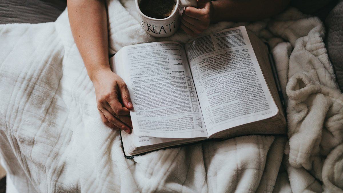 A person holding a cup of coffee while reading a book in the morning