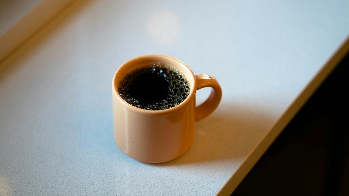 A mug of black coffee on a table in afternoon light