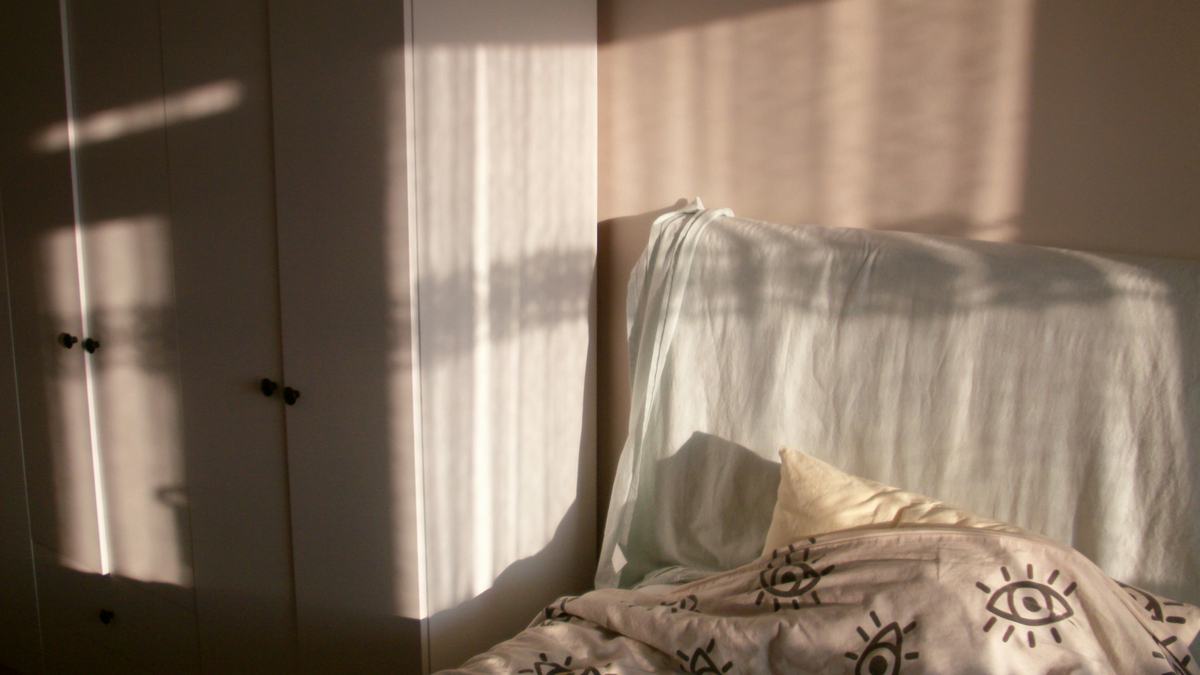 Morning sunlight streaming across an unmade bed through a bright window
