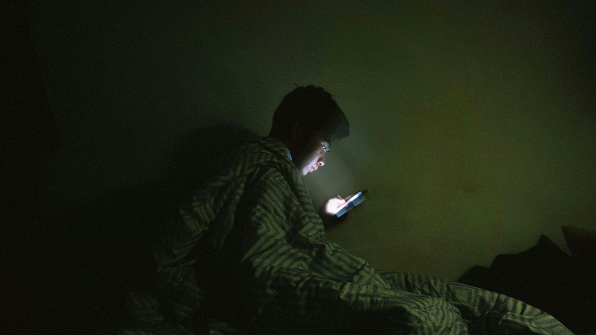A person sitting up in a dark bed, face lit by a phone screen