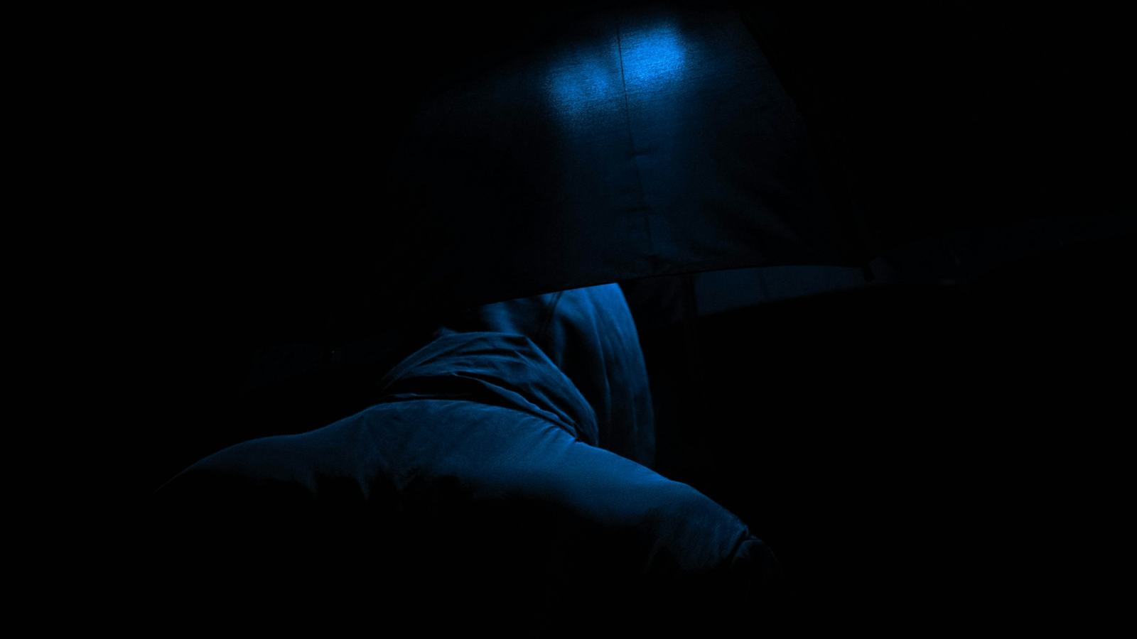 A person asleep in a dark bedroom at night, lit only by a faint blue glow