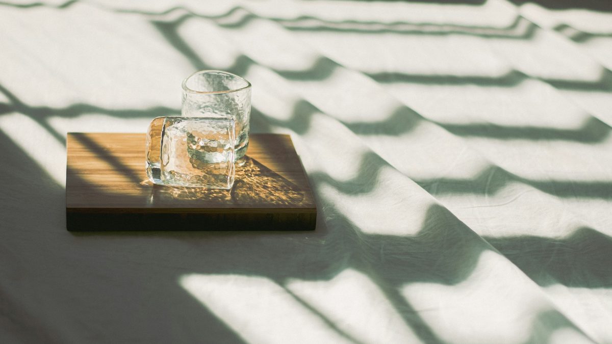 A glass of water on a wooden board in stripes of morning sunlight