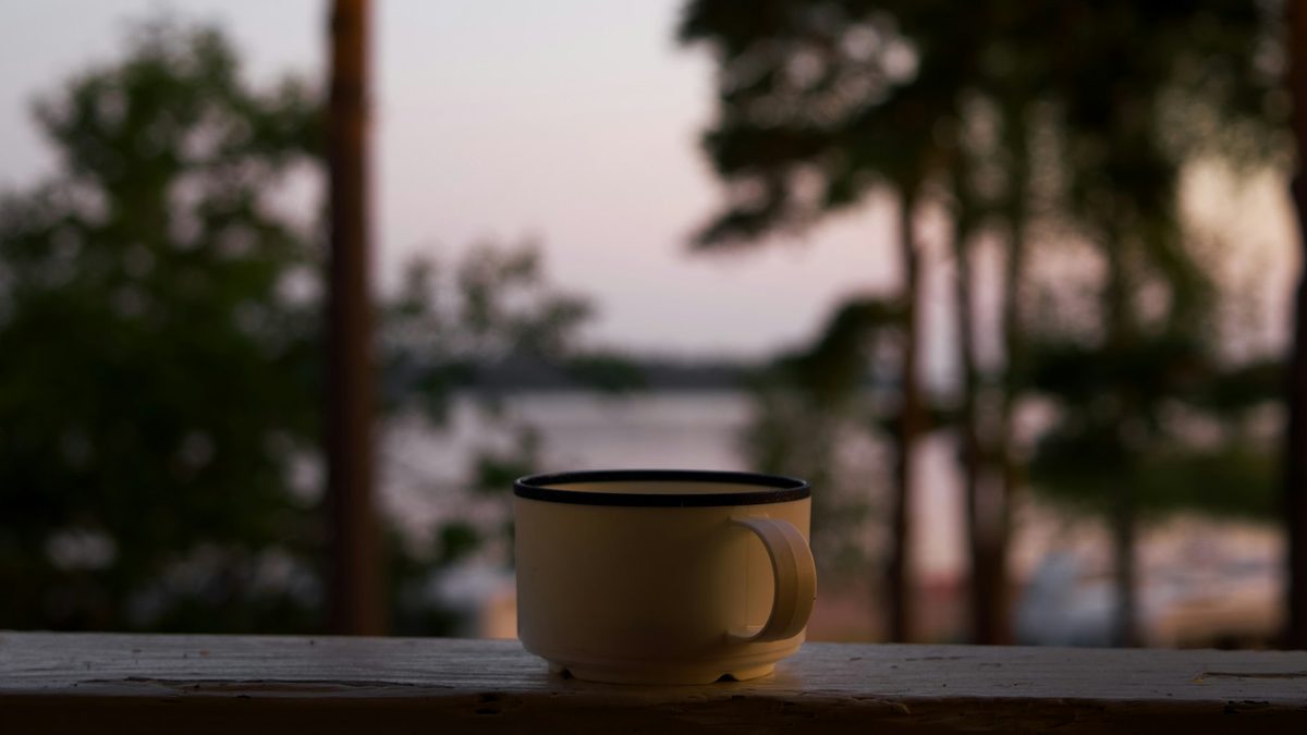 A cup of coffee on a wooden railing at dusk