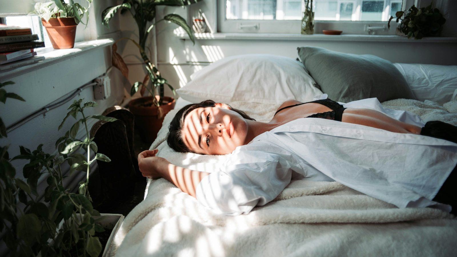 A woman in a white robe asleep on a bed in bright late-morning light