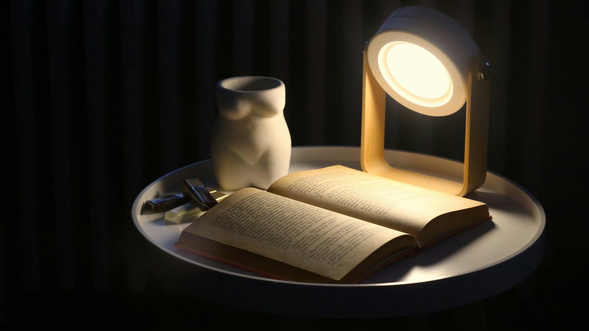An open book and a warm reading lamp on a bedside table
